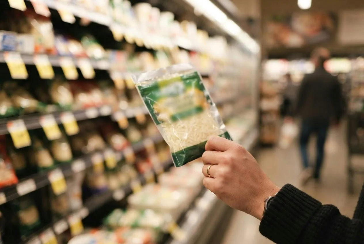 Hand pakt een pak geraspte vegan kaas uit het koelvak in de supermarkt